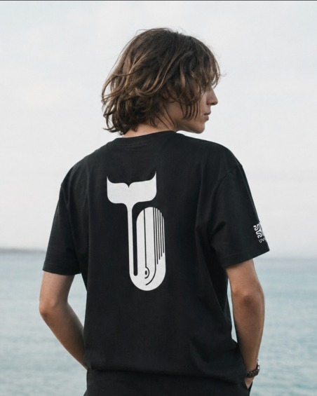 Homme de dos sur la plage portant le tee-shirt UVEA WHALE gris foncé, queue de baleine blanche imprimée au dos