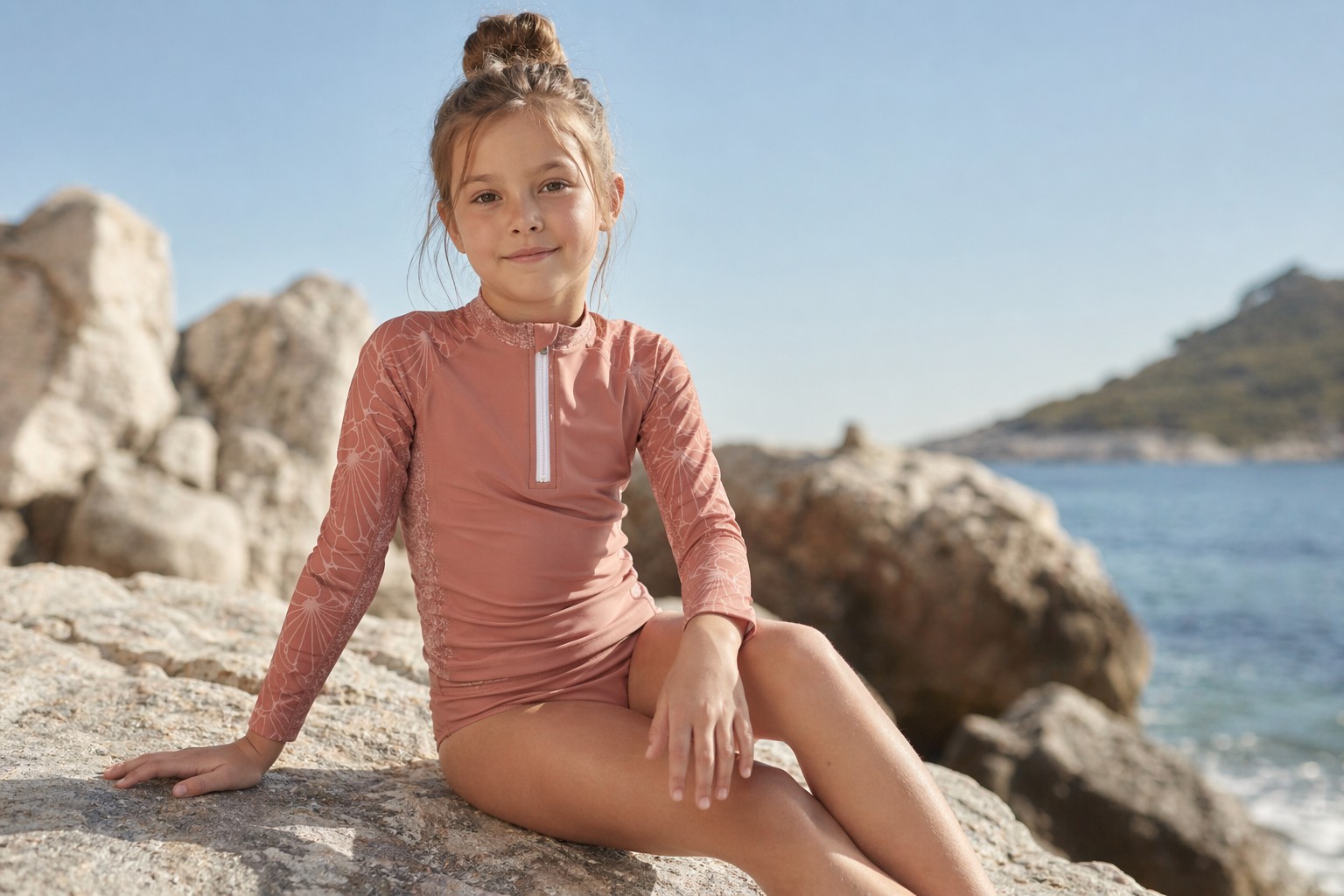 Petite fille en rashguard UVEA assise au bord de mer