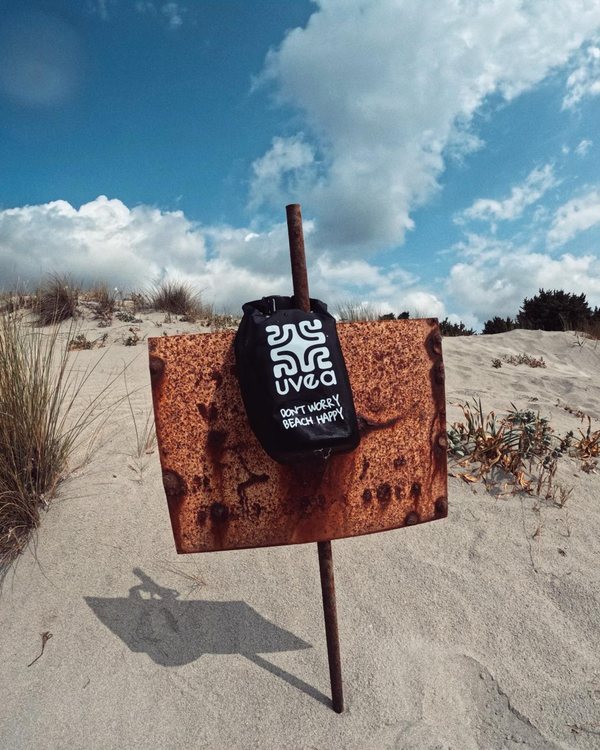 Schwarzer UVEA Dry Bag auf einem Schild in den Dünen
